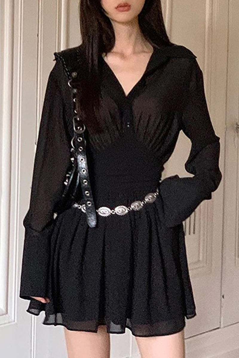 A woman wearing a black sheer dress with a cinched waist and flared sleeves, accessorized with a silver belt.