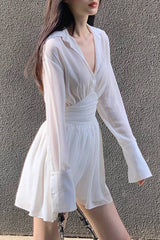 A woman wearing a white sheer dress with a cinched waist and flared sleeves.