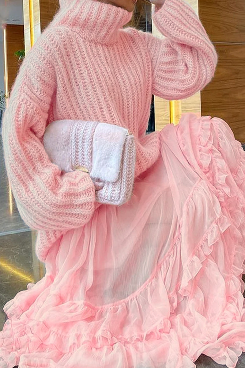 Close-up of a person wearing a pink chunky knit turtleneck sweater with voluminous sleeves.