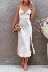 Woman in a white satin slip dress with spaghetti straps and a side slit, holding a tan clutch.