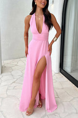 A woman in a pink halter maxi dress with a deep V-neck and a high slit on the leg.
