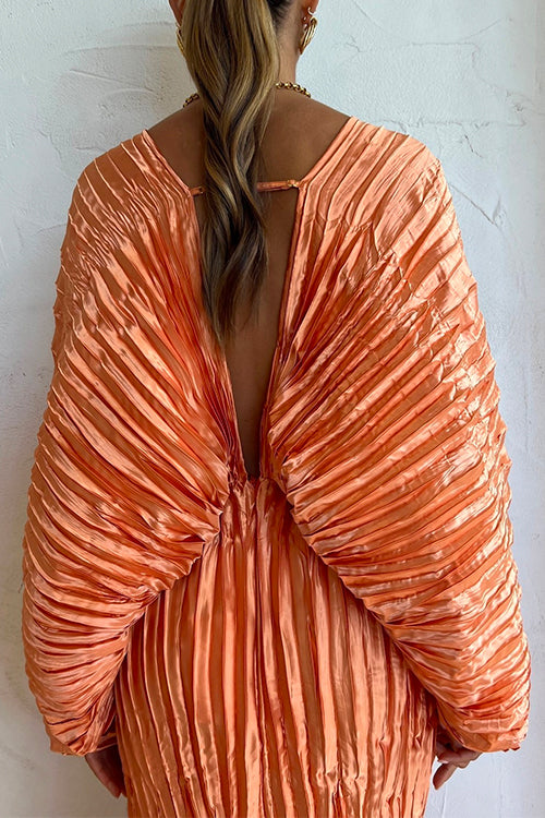 Back view of a woman wearing an orange pleated maxi dress with a deep V-neckline and voluminous sleeves, showing an open back.