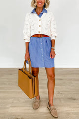 Woman wearing a blue and white striped shirt dress belted with a brown belt, a white textured cardigan, and brown loafers.