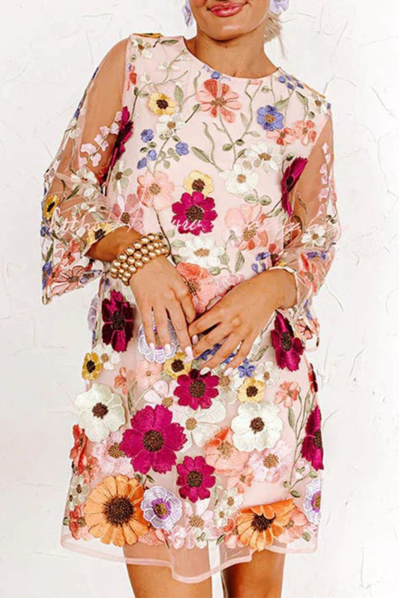 A woman in a pink floral embroidered sheer mini dress with bell sleeves.