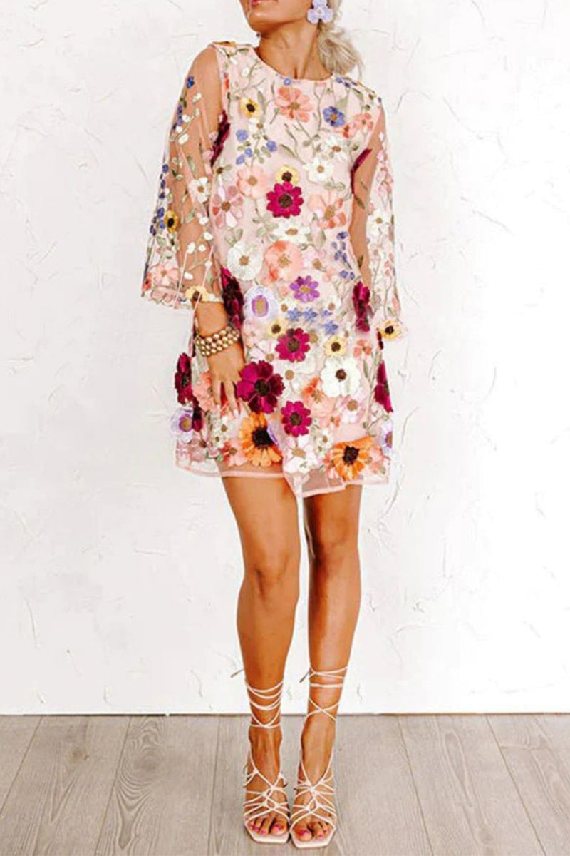 Full body shot of a woman in a pink floral embroidered sheer mini dress and white lace-up heels.
