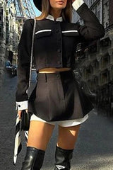Woman wearing a black cropped jacket and skirt set with white trim and boots, standing on a city street.
