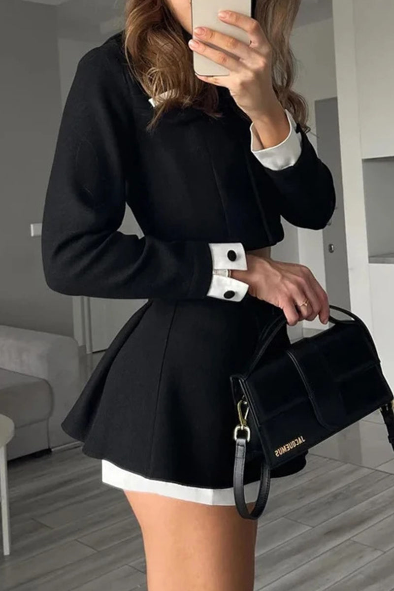 Woman holding a black handbag and showing off the details of a black cropped jacket and skirt set with white cuffs.