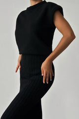 Close-up of a woman wearing a black ribbed knit sleeveless top and a black ribbed knit midi skirt.