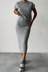 A woman wearing a grey ribbed knit sleeveless top and a grey ribbed knit midi skirt with sneakers.