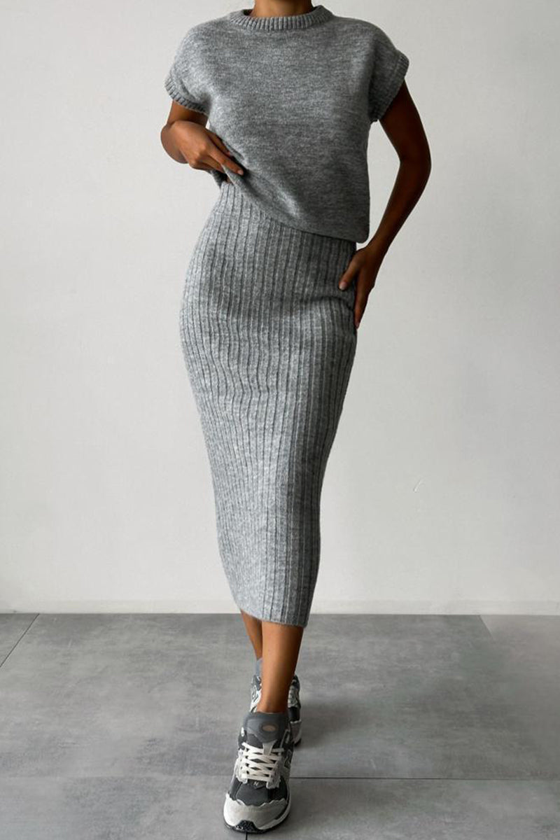 A woman wearing a grey ribbed knit sleeveless top and a grey ribbed knit midi skirt with sneakers.