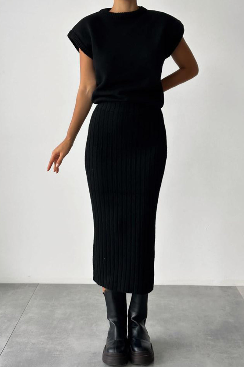 A woman wearing a black ribbed knit sleeveless top and a black ribbed knit midi skirt with black boots.