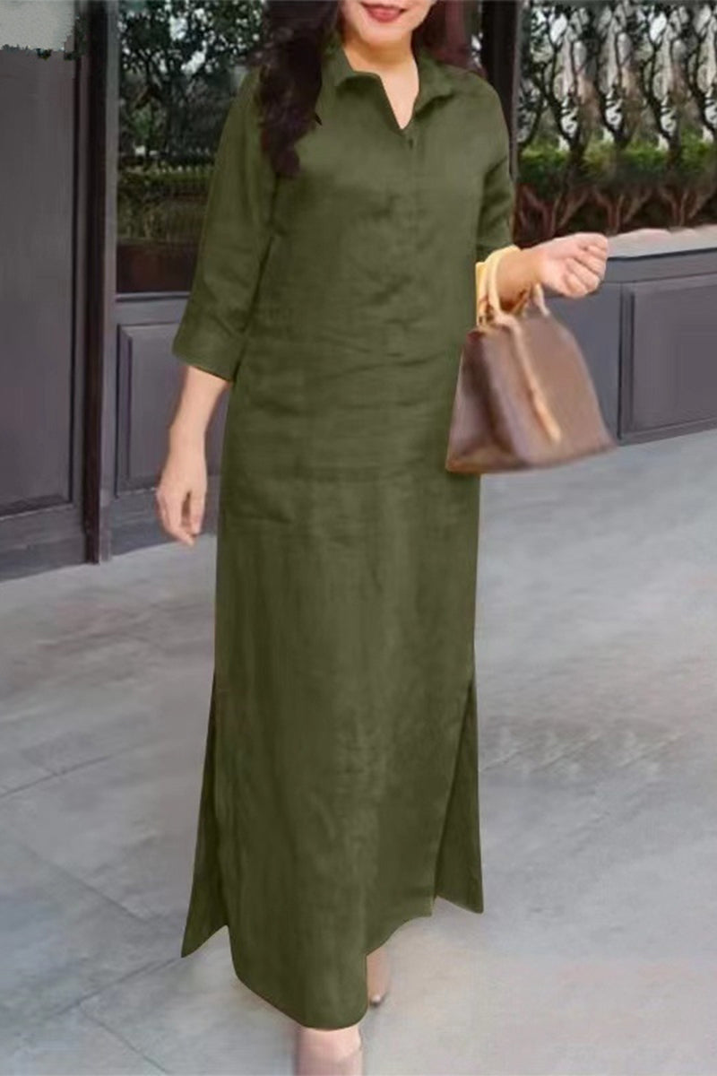 A woman stands wearing a long green dress with a collared neckline and three-quarter sleeves.