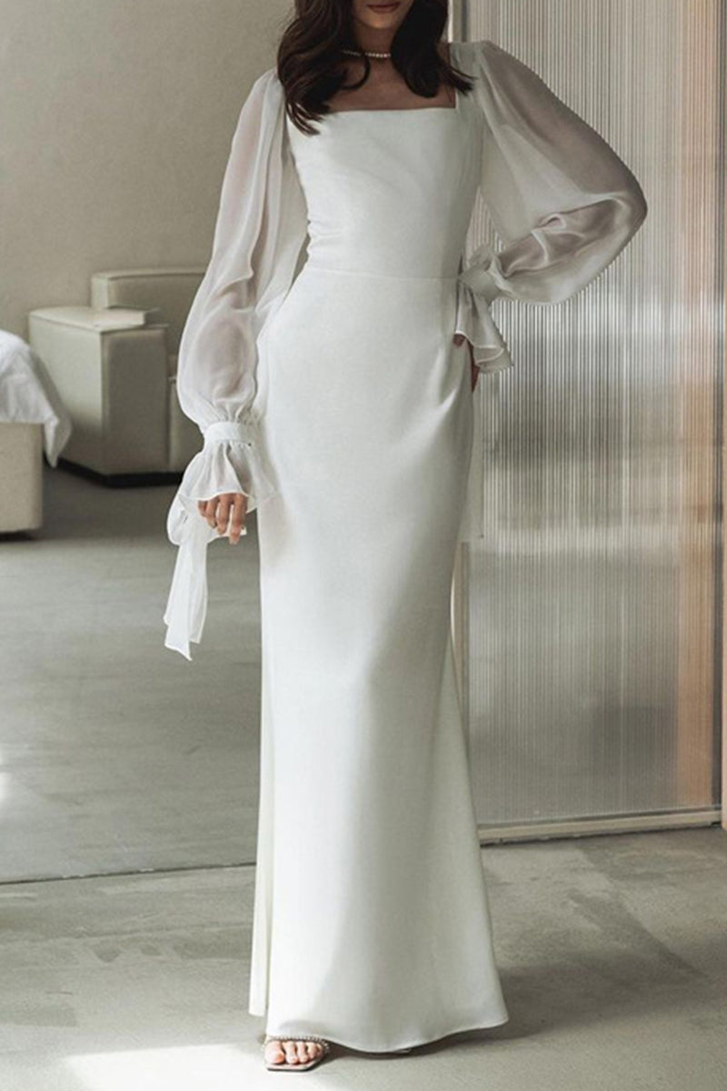 Woman in a white long dress with sheer bishop sleeves and a square neckline, standing with one hand on her hip.
