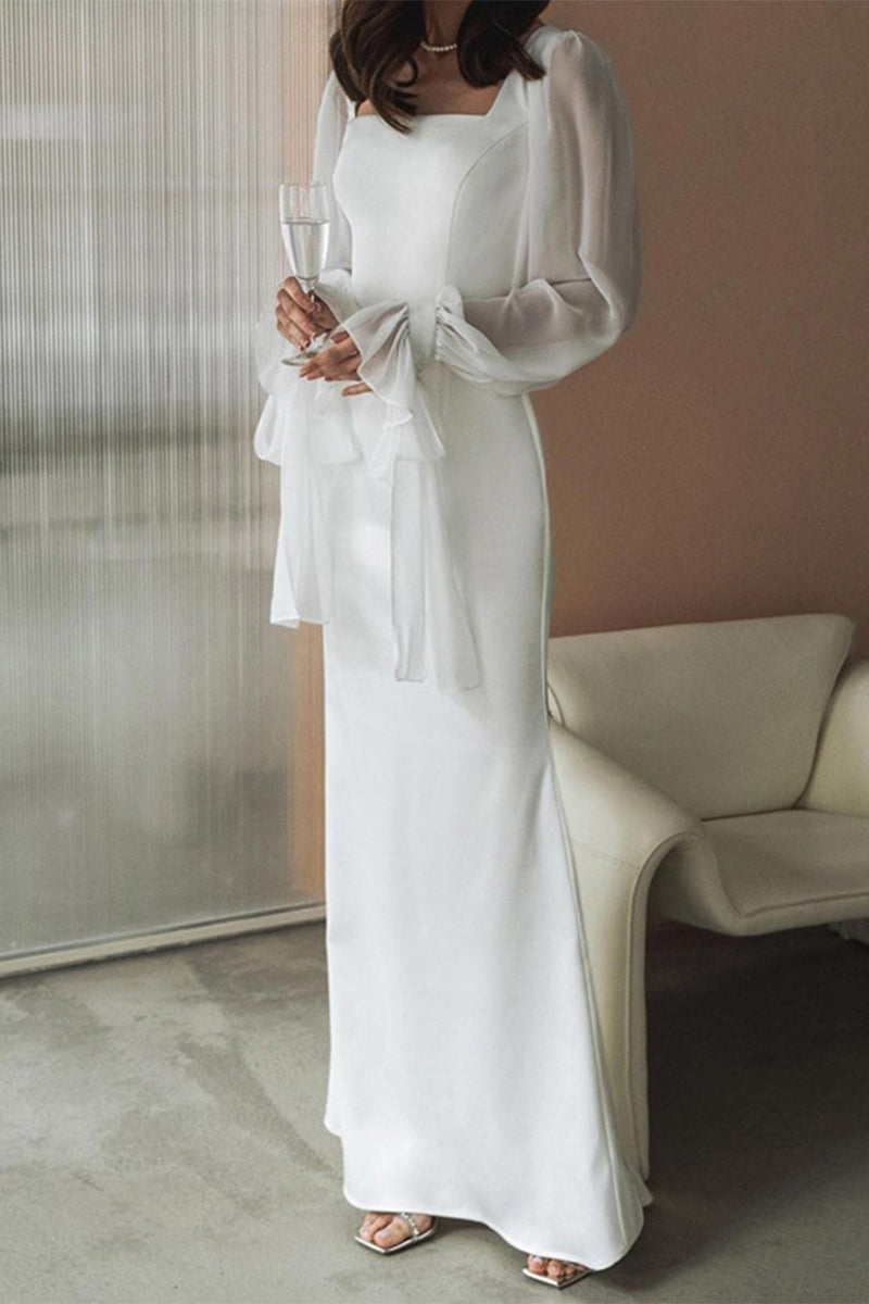 Woman in a white long dress with sheer bishop sleeves and a square neckline, holding a glass of champagne.