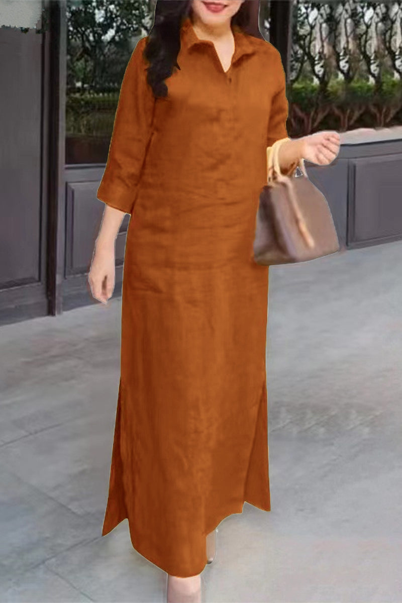 A woman stands wearing a long brown dress with a collared neckline and three-quarter sleeves.