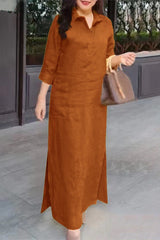 A woman stands wearing a long brown dress with a collared neckline and three-quarter sleeves.