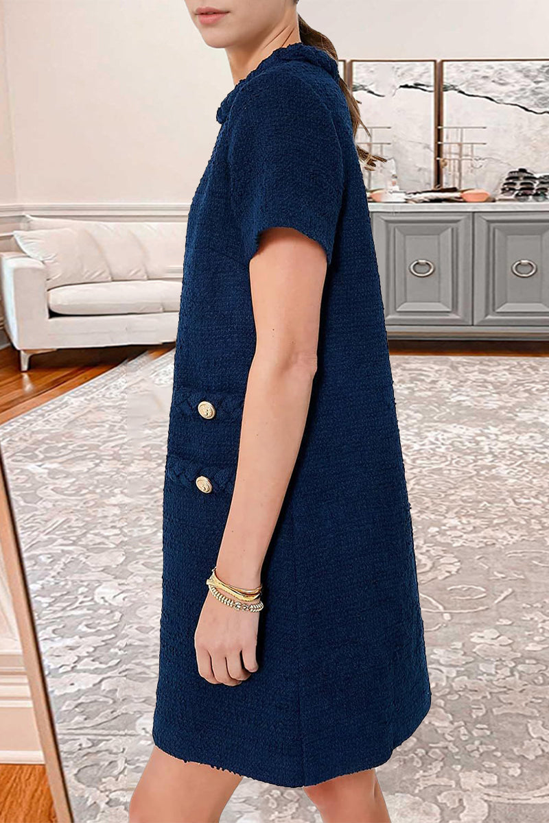 Side view of a woman wearing a navy blue textured A-line shift dress with short sleeves, a ruffled neckline, and decorative pockets. She is wearing layered bracelets.
