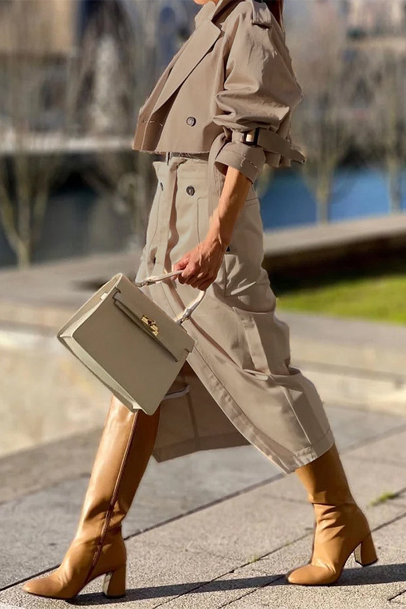Woman walking with a cream handbag, wearing a tan cropped jacket and matching asymmetrical skirt with tan boots