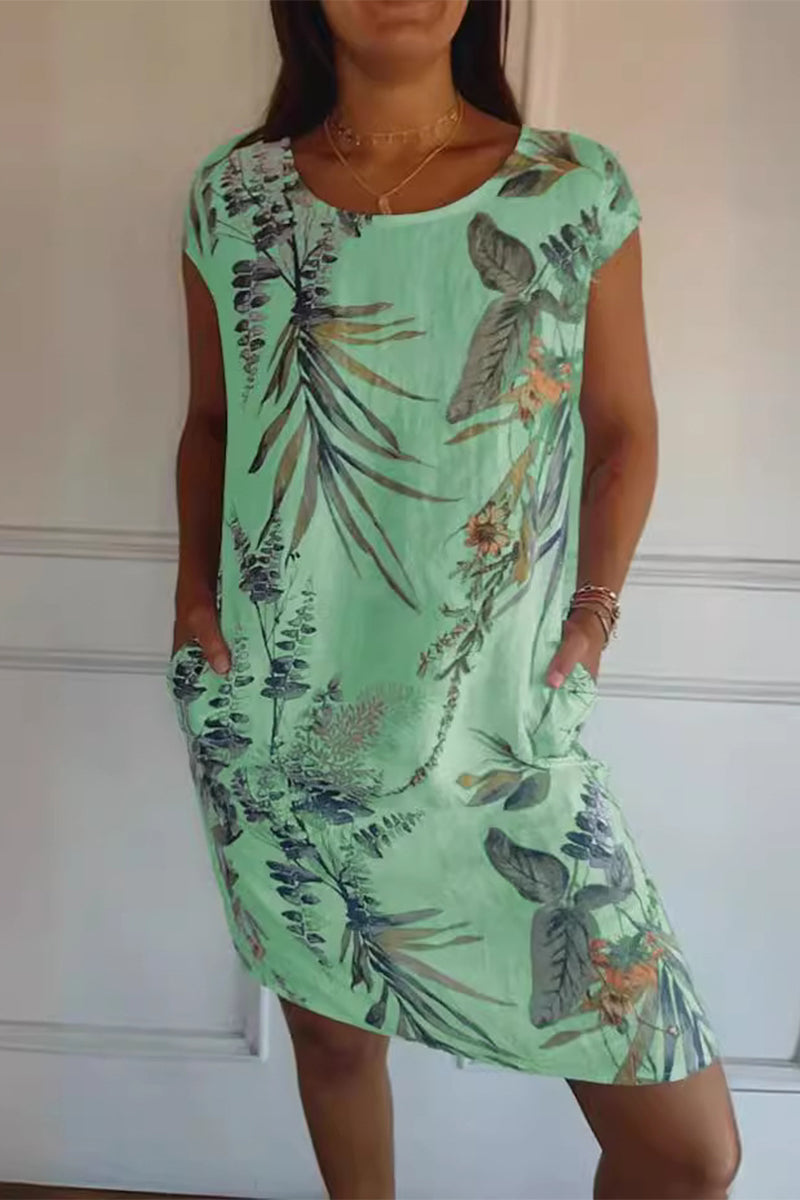 A woman wearing a green floral print cap sleeve dress with pockets.
