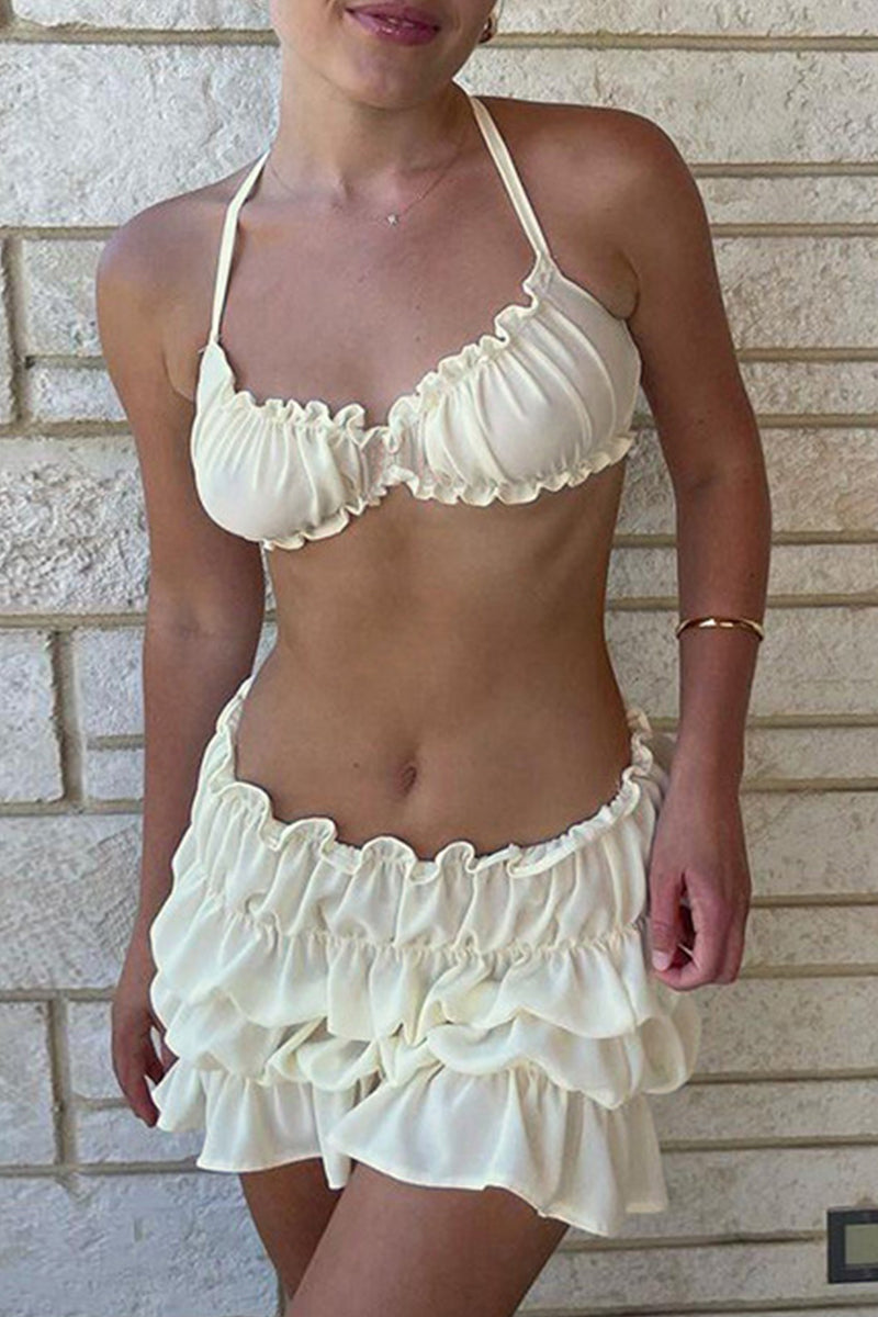 Woman wearing a white ruffled bikini and skirt against a brick wall