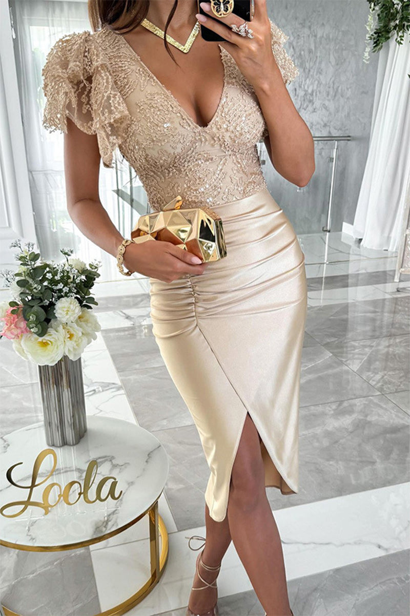 Woman in a gold sequined and lace v-neck dress with a ruched satin skirt and a high slit, holding a gold clutch.