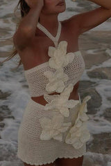 A woman in a white crochet bikini set with large white floral appliqués, standing in the ocean.