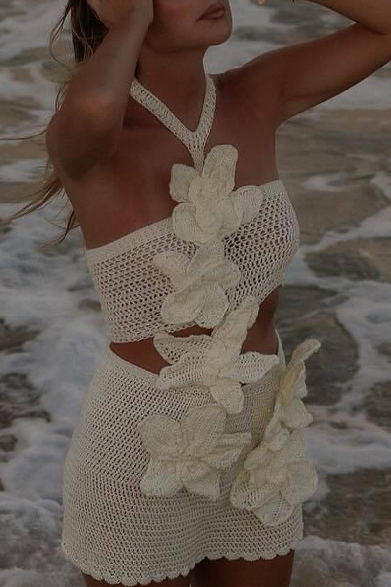 A woman in a white crochet bikini set with large white floral appliqués, standing in the ocean.