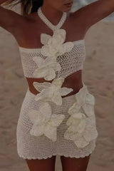 A woman in a white crochet bikini set with large white floral appliqués, standing on a sandy beach.