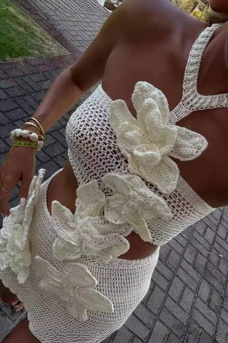 Close-up of a woman wearing a white crochet crop top with floral appliqués and a matching mini skirt.