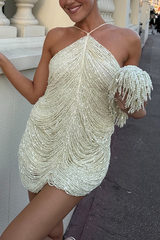 A woman in a cream-colored beaded mini dress with a halter neckline and fringe details, holding a matching clutch.