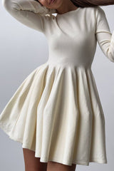 A woman in a long-sleeved ivory fit-and-flare dress with her arms raised.
