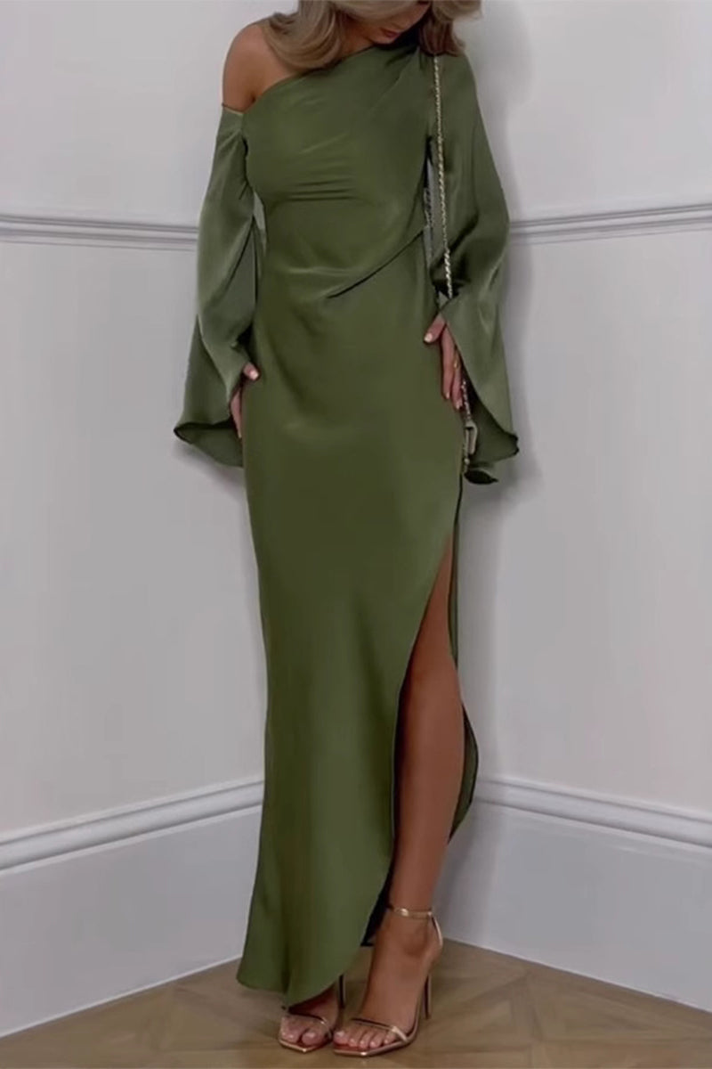 A woman stands in a corner wearing a flowing olive green satin dress with a one-shoulder design and dramatic bell sleeves. The dress features a high slit on the side, revealing her leg, and she is wearing gold strappy heels.