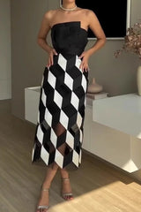 A woman stands with her hands on her hips wearing a black and white geometric print sheath dress.