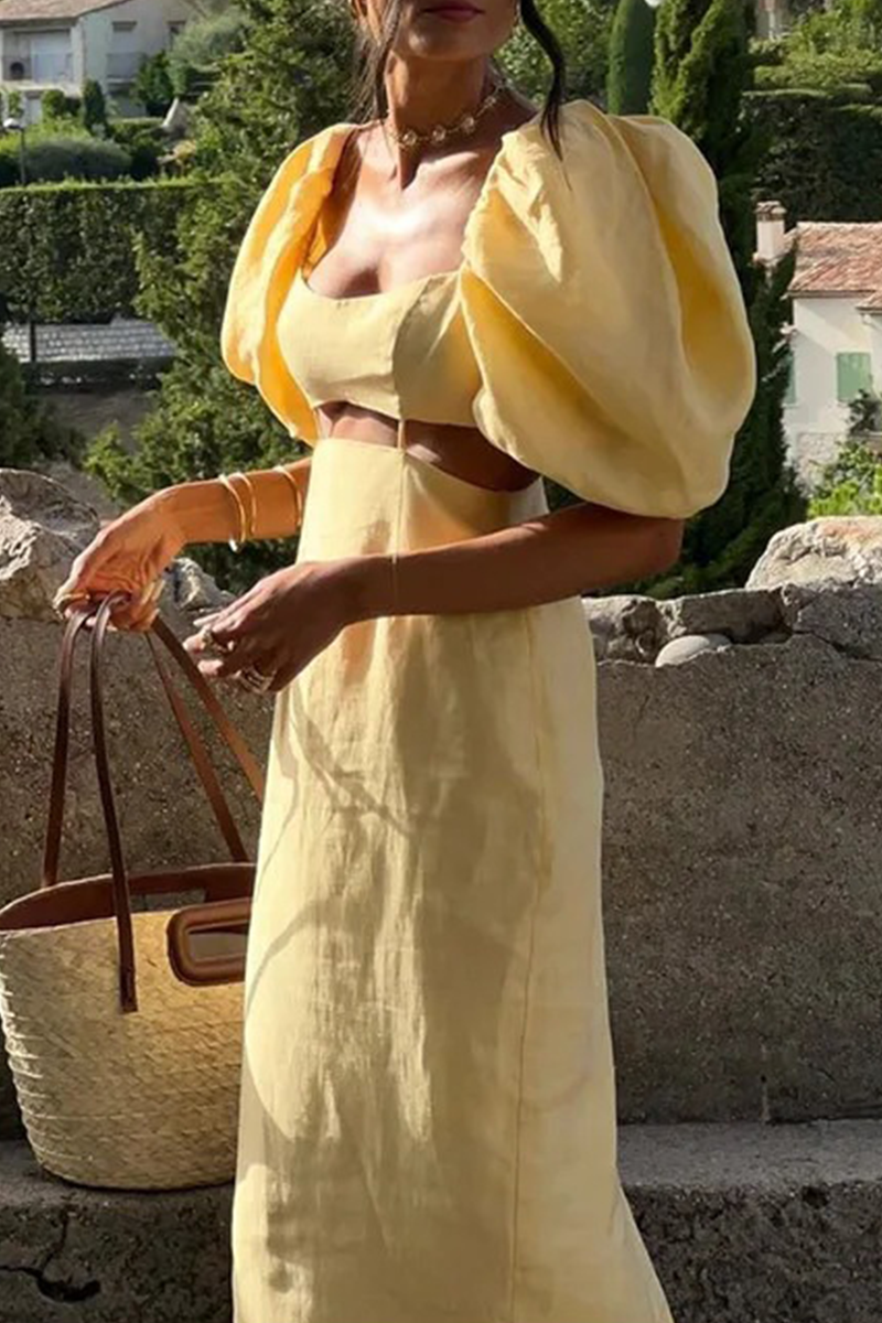 A woman wearing a yellow linen dress with puff sleeves and a cut-out detail, sitting on a stone wall.