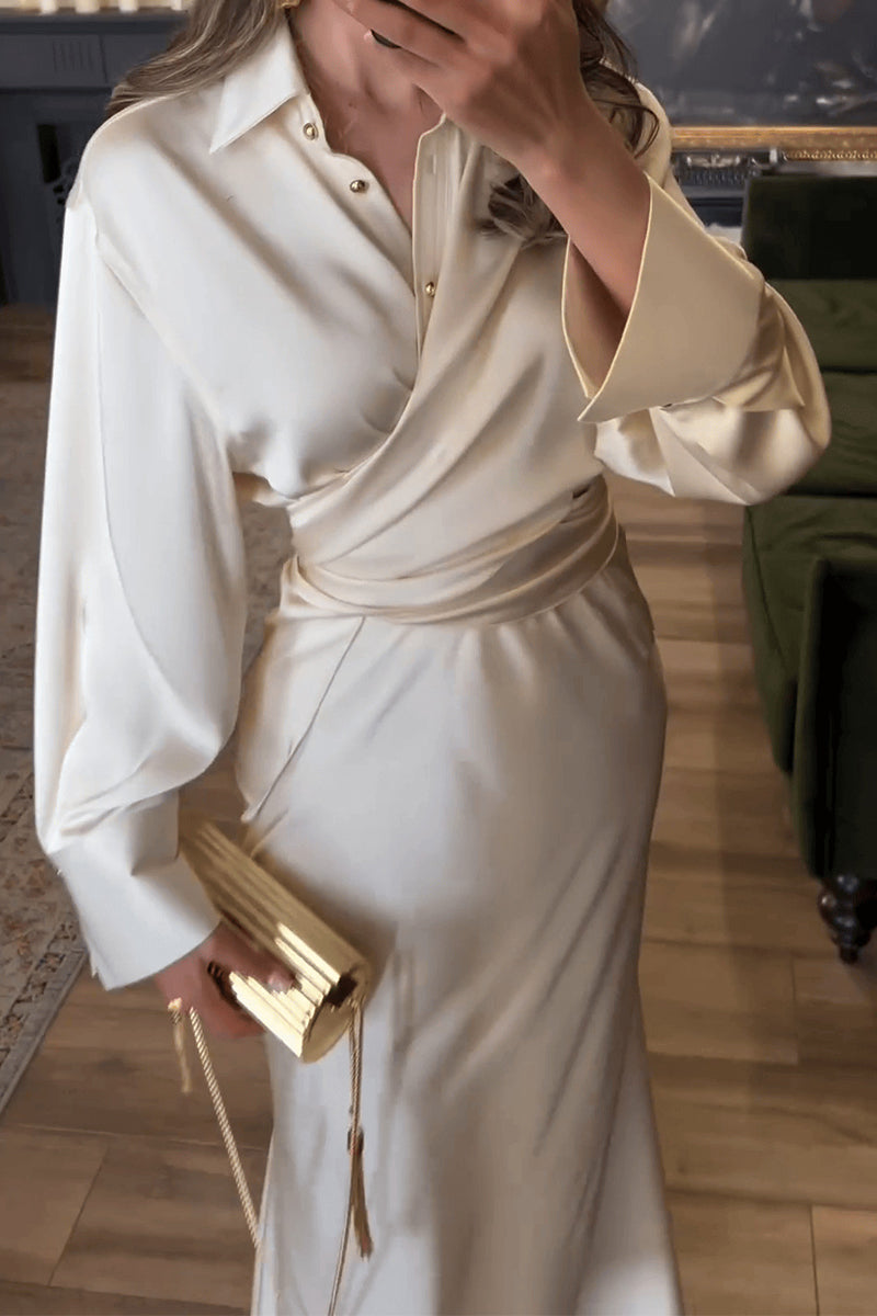 A woman in a flowing ivory satin wrap dress with a matching belt, accessorized with a metallic gold clutch.