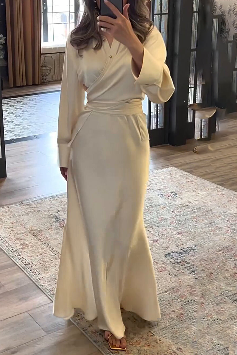 Full-length shot of a woman in an elegant ivory satin wrap dress with a mermaid hem, holding a gold clutch.