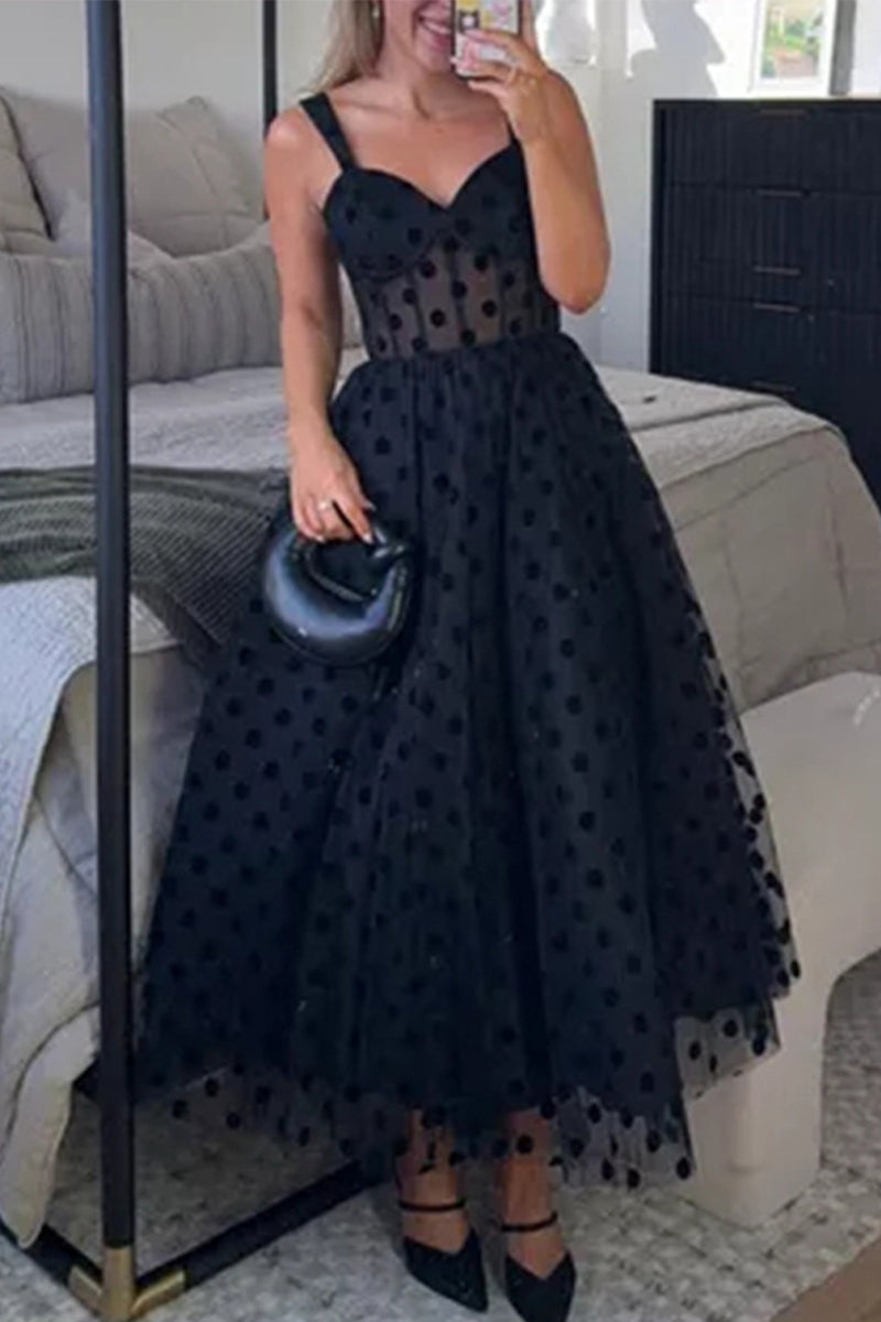 Woman wearing a black polka dot tulle midi dress with a sweetheart neckline and spaghetti straps, holding a black clutch.