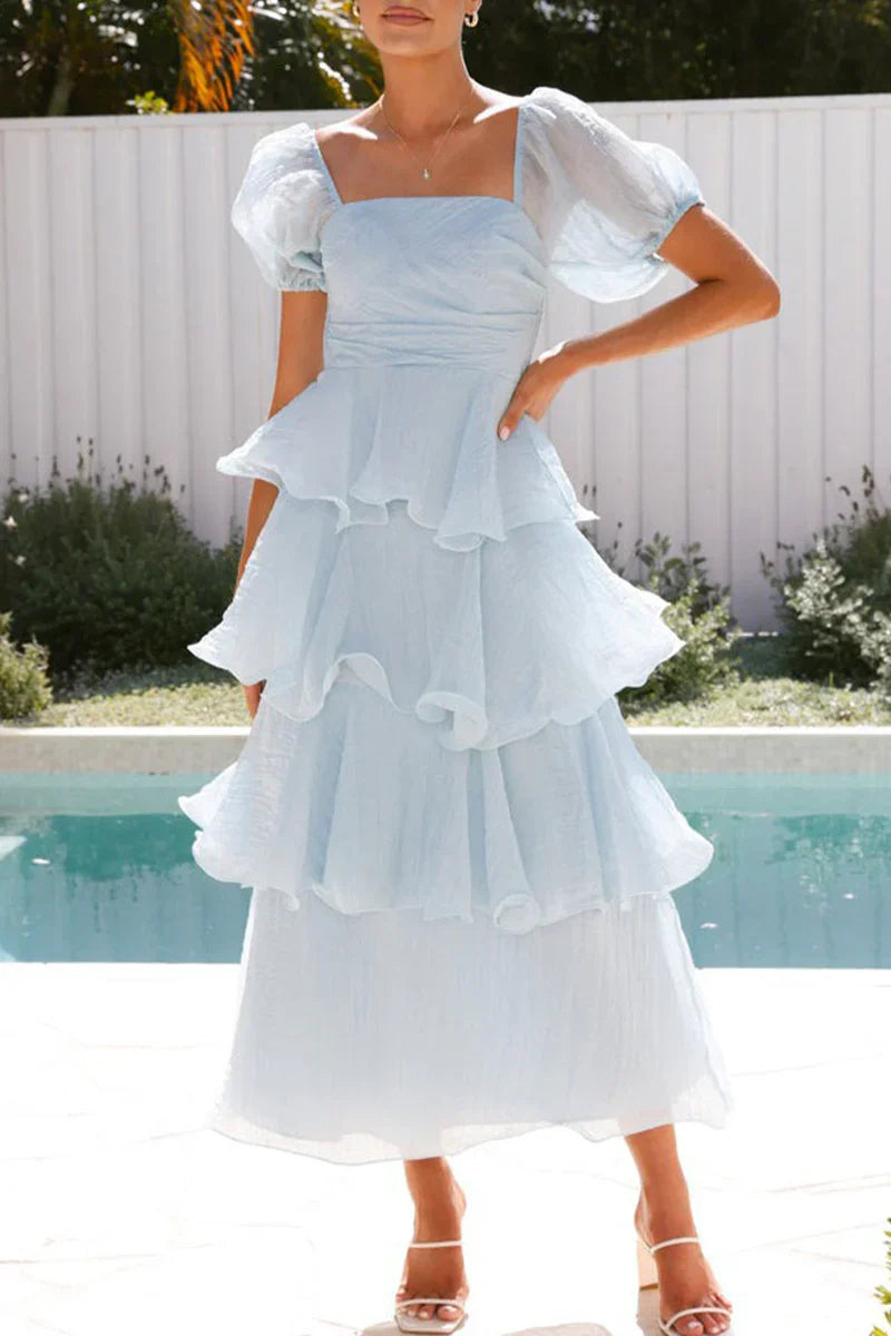 Woman wearing a light blue tiered ruffle dress with puff sleeves standing by a pool.