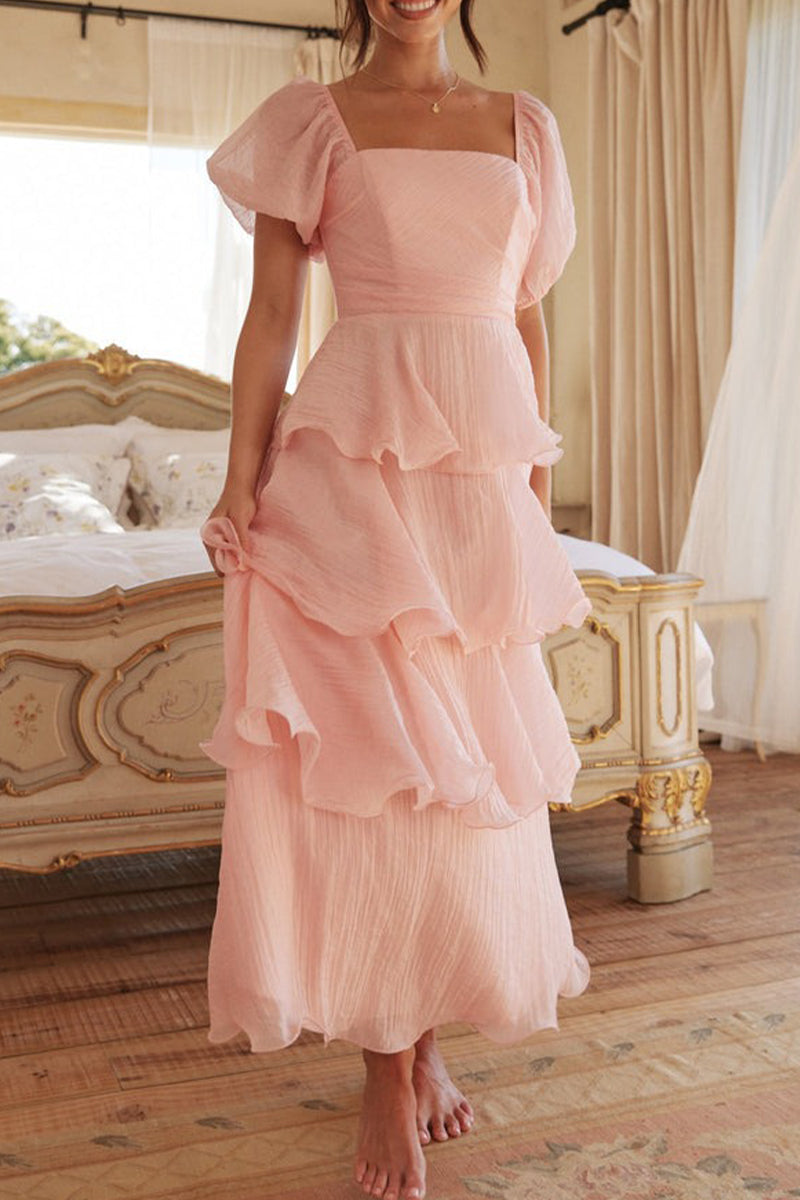 Woman wearing a pink tiered ruffle dress with puff sleeves standing in a bedroom.