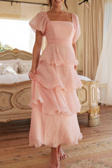 Woman wearing a pink tiered ruffle dress with puff sleeves standing in a bedroom.
