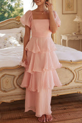 Woman in a pink tiered ruffle dress with puff sleeves touching her hair.