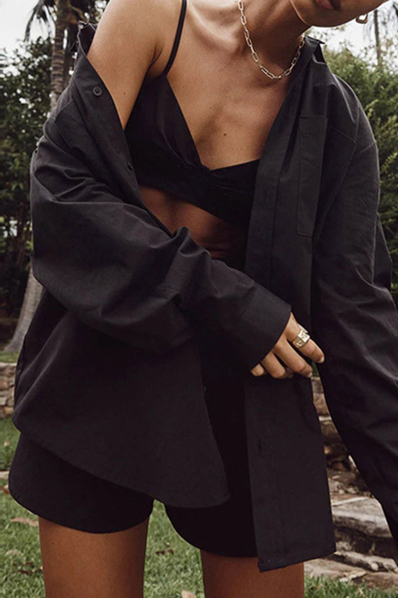 Model wearing a black oversized button-up shirt over a black bralette and shorts.