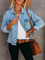 Close-up of a woman wearing a light blue distressed denim jacket, white tank top, brown belt, and layered necklaces.