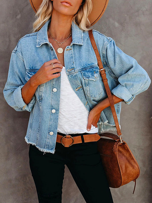 Close-up of a woman wearing a light blue distressed denim jacket, white tank top, brown belt, and layered necklaces.