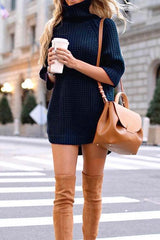 Woman wearing a navy blue turtleneck sweater dress with tan thigh-high boots and a tan handbag