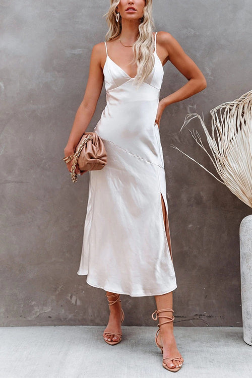 Woman in a white satin slip dress with spaghetti straps and a side slit, holding a tan clutch.
