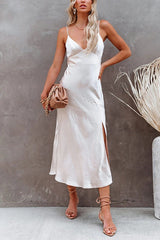Woman in a white satin slip dress with spaghetti straps and a side slit, holding a tan clutch.