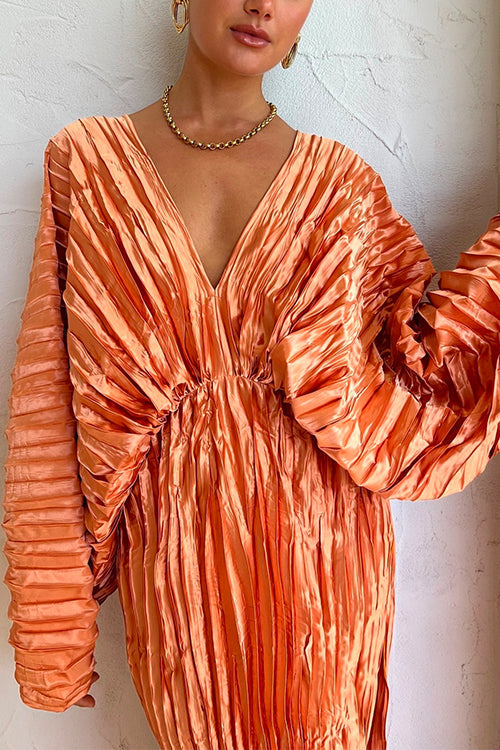Close-up of a woman wearing an orange pleated maxi dress with a deep V-neckline and long sleeves, showcasing the fabric texture.