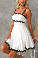 Front view of a woman wearing a white fit and flare mini dress with black scalloped trim on the straps and hem.