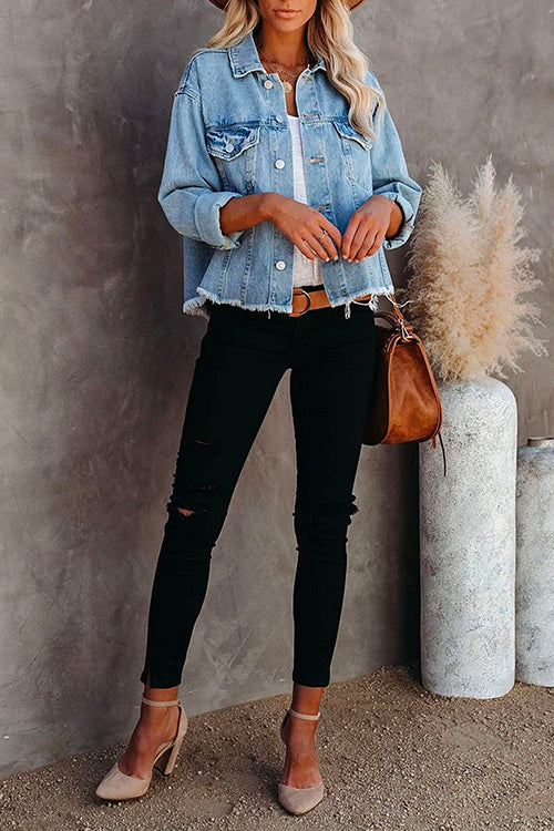 Full body shot of a woman in a light blue distressed denim jacket, white tank top, black ripped jeans, brown belt, and nude heels.